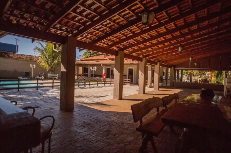 Área coberta com mesas de madeira rústica e vista para a piscina no fim da tarde