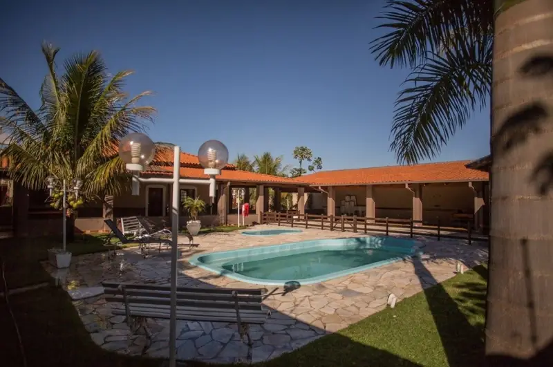 Área da piscina com luminárias de globo, deque de pedra, palmeiras e as varandas ao fundo