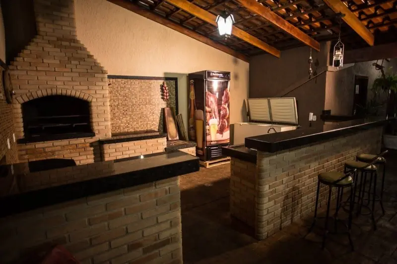 Área gourmet com churrasqueira, balcão de bar em granito e banquetas