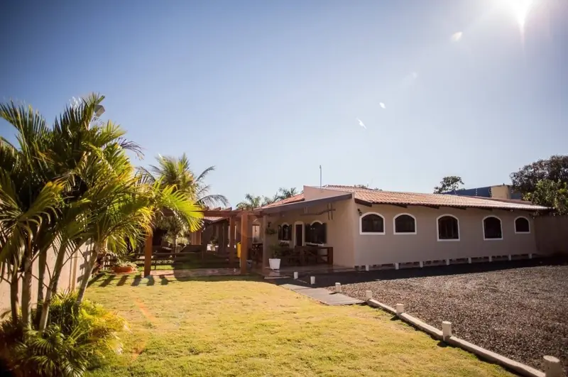 Casa das suítes com janelas em arco, gramado e palmeiras em dia de sol