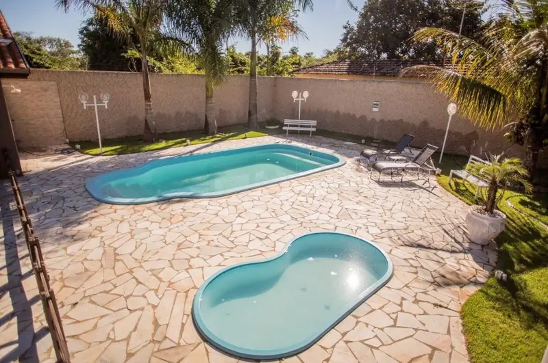 Vista das duas piscinas, adulto e infantil, com deque de pedra e espreguiçadeiras