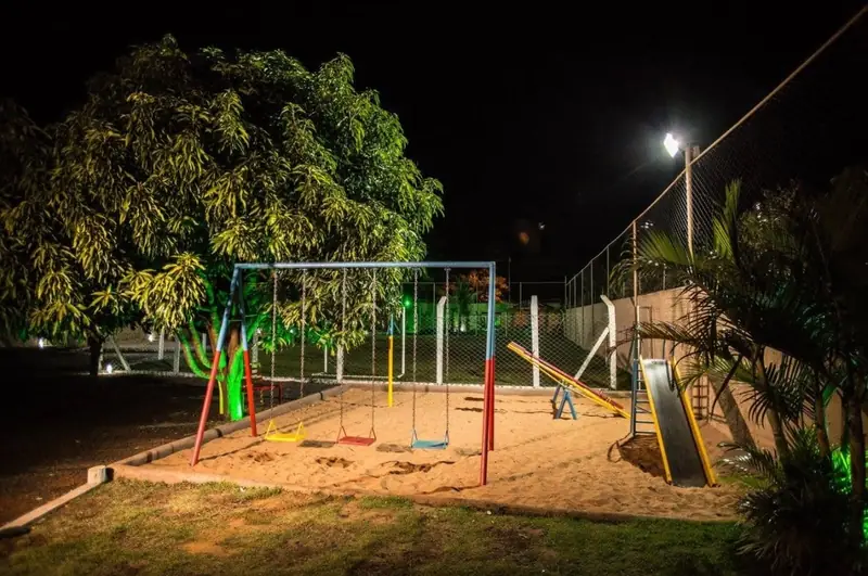 Parquinho com balanços e escorregador na areia, iluminado à noite