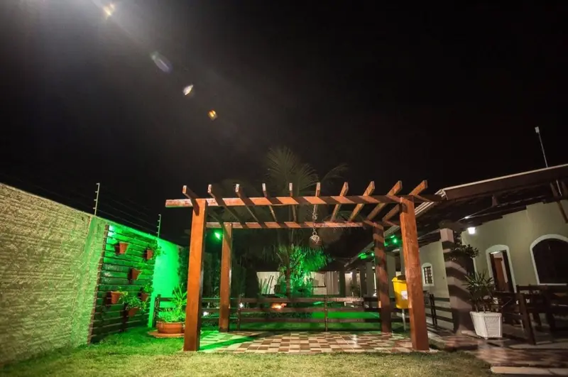Pérgola de madeira iluminada à noite, junto à varanda da casa