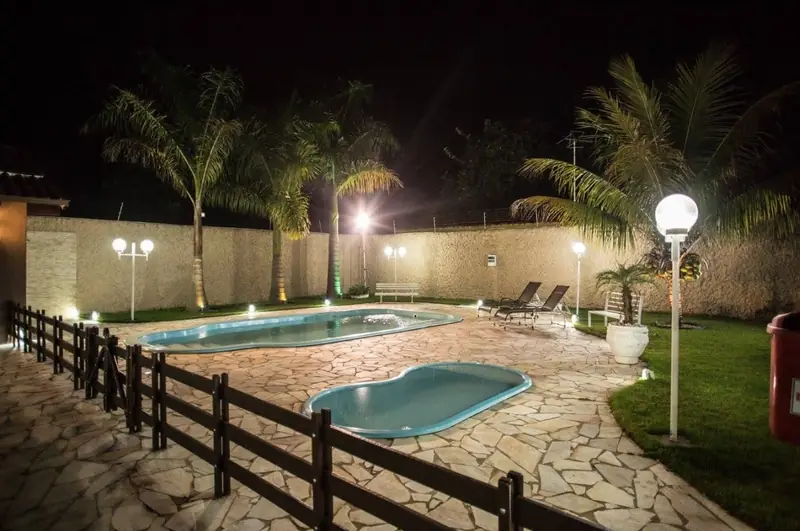 Piscina adulto e piscina infantil iluminadas à noite, com luminárias e palmeiras