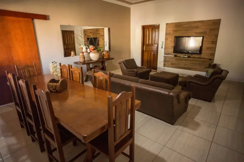Sala de estar com sofás e TV em painel de madeira e mesa de jantar de madeira