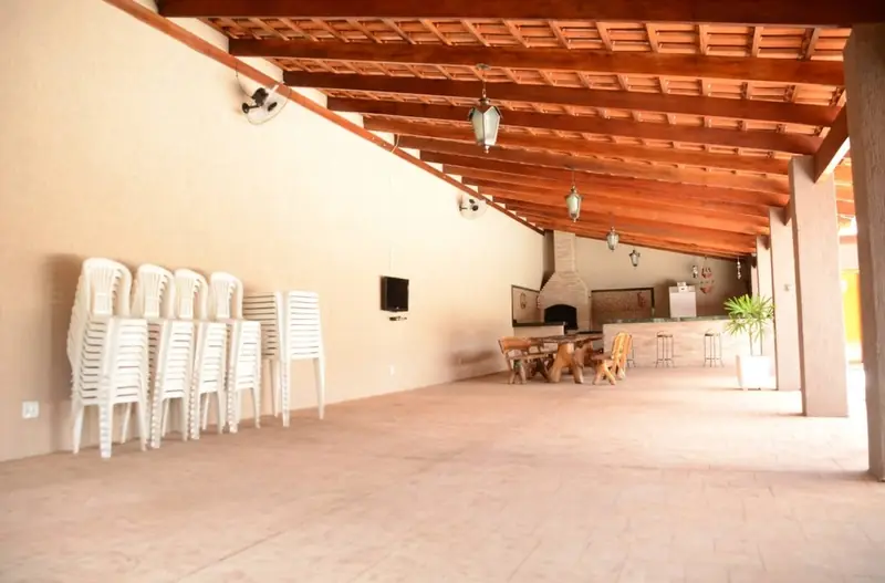 Salão coberto para festas com forro de madeira, ventiladores, cadeiras empilhadas e mesas ao fundo