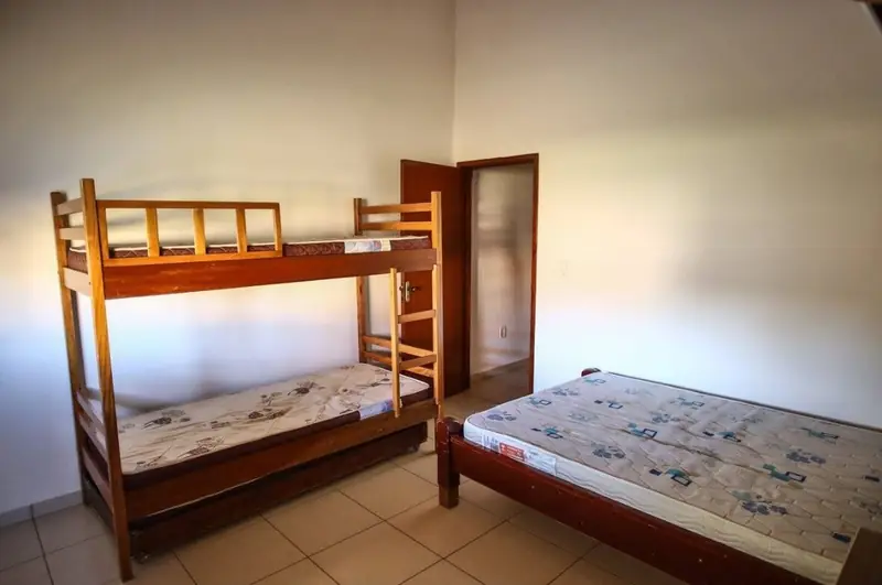 Suíte com beliche de madeira, cama de casal e porta do banheiro