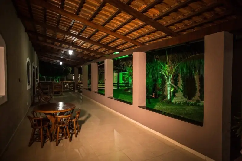 Varanda coberta com mesas de madeira e o jardim iluminado à noite